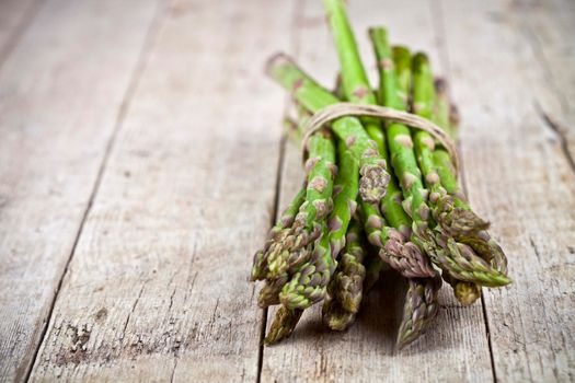 Bunch of fresh raw garden asparagus on rustic wooden table background. Green spring vegetables. 