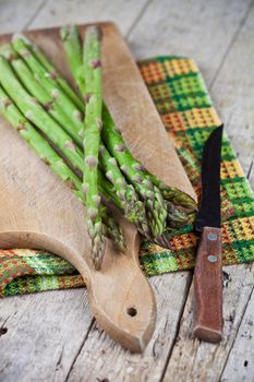 Raw garden asparagus and knife closeup on cutting board on rustic wooden table background. 