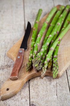Fresh raw garden asparagus and knife closeup on cutting board on rustic wooden table background. Green spring vegetables. 