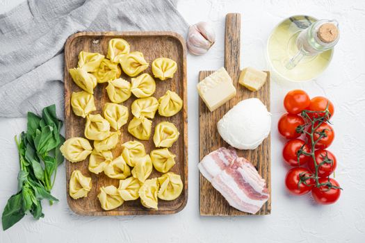 Italian Homemade Tortellini with ingredients, ham, basil, pesto, mozzarella, on wooden tray, on white background, top view flat lay