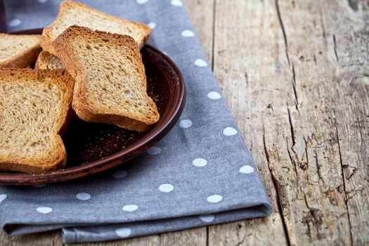 Toasted cereal bread slices on brown ceramic plate closeup on linen napkin on rustic wooden table background.