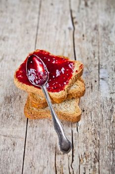 Toasted cereal bread slices stack with homemade cherry jam and spoon closeup on rustic wooden table background. 