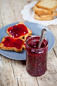 Homemade cherry jam and fresh toasted cereal bread slices plates closeup on rustic wooden table background.