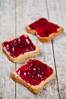 Toasted cereal bread slices with homemade cherry jam closeup on rustic wooden table background.