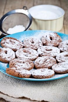Fresh baked chocolate chip cookies with sugar powder on blue plate and metal strainer closeup on rustic wooden table.