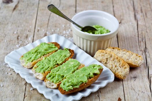 Crostini with avocado guacamole on white plate closeup on rustic wooden table. Diet breakfast.