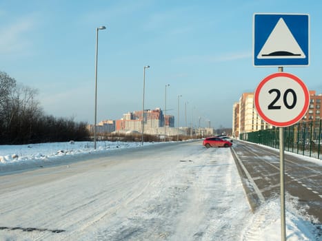 A snowy street with the established traffic signs 5.20 "Artificial roughness" and 3.24 "Restriction of the maximum speed" 20 km