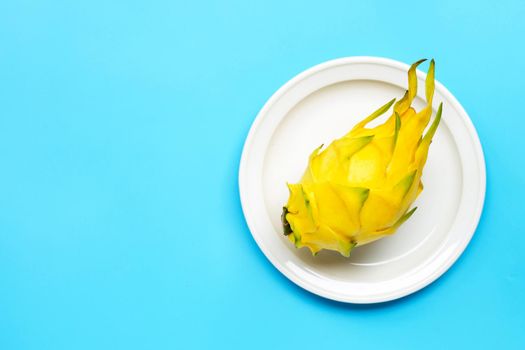 Yellow pitahaya or dragon fruit on white plate on blue background. 