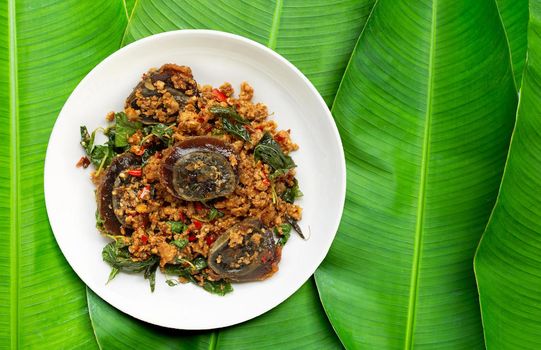 Thai food. Stir-fried minced pork, preserved egg  with basil leaves on banana leaves background.