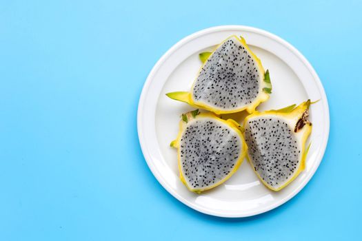 Yellow pitahaya or dragon fruit on white plate on blue background.