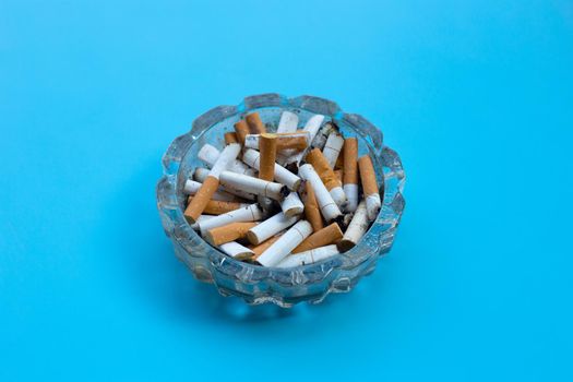 Cigarette butts in glass ashtray on blue background.
