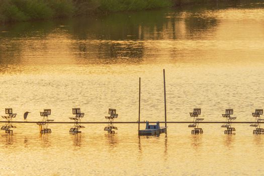 paddle wheel or aeration machine with heron bird in shrimp farm by silhouette