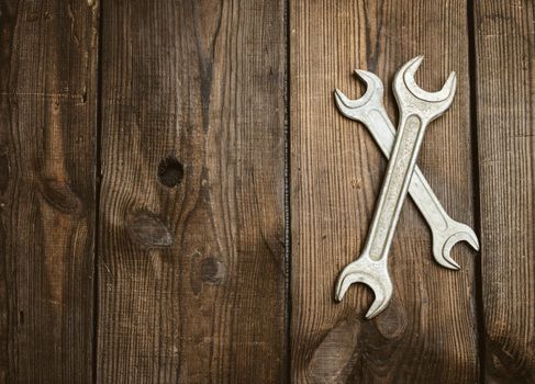 two metal adjustable wrenches on a brown wooden background