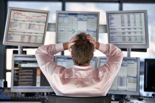 Rear view of stressed stock trader looking on computer screens