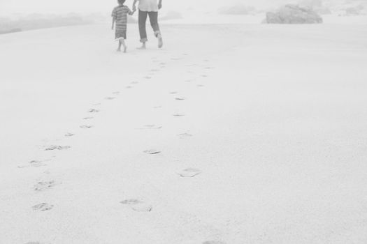 Black and white photo of mother and son walking on the beach barefoot