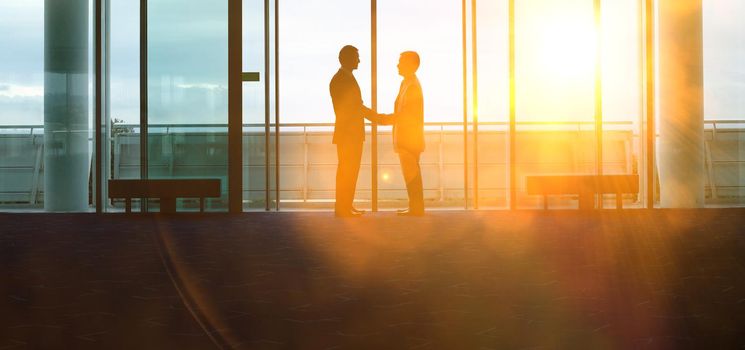 Two silhouette businessmen shaking hands in the airport lobby