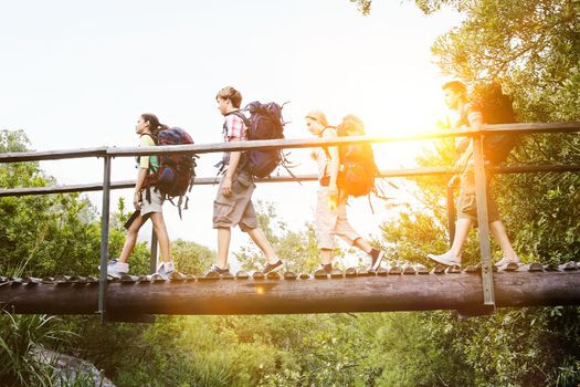 Teenage boys and girls with backpacks walking on bridge in forest