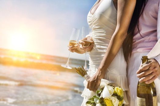Midsection of newlywed couple with champagne bottle and flutes on beach
