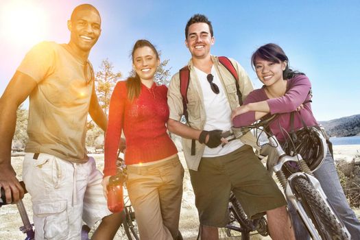 Portrait of four multiethnic young friends standing on lake shore with mountain bikes