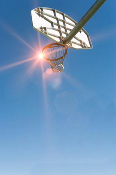 Low angled view of a basket ball net and hoop and backboard with strong sunshine lens flare