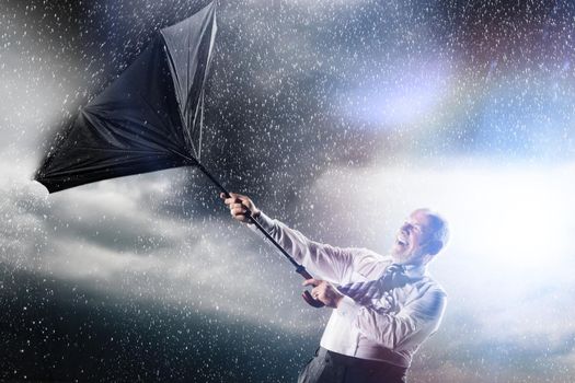 Businessman losing control of inside out umbrella