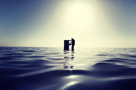 Businessman Standing in the Ocean Searching Through a Filing Cabinet