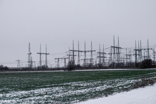 Electric substation on the background of a green field with winter wheat and snow in winter.