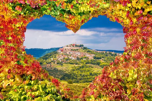 Historic town of Motovun on green hill view through heart shaped autumn leaves
