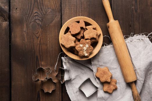 baked star shaped gingerbread cookies, wooden rolling pin and metal cutters on a black table