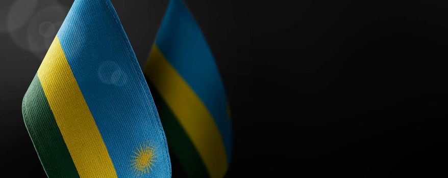 Small national flags of the Rwanda on a dark background