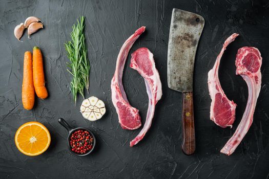 Frenched raw fatty lamb chops, with ingredients carrot orange, herbs, on black stone background, top view flat lay