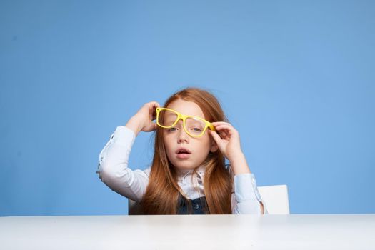 red-haired girl with yellow glasses sitting at the table emotions education