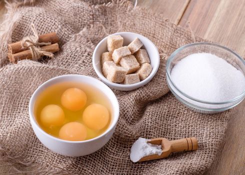 baking ingredients eggs, sugar, baking powder,  cinnamon for baking on a wooden table