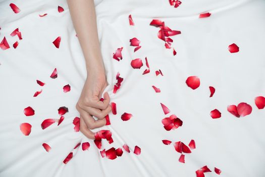 Women hand pulling or grasping white sheets. Hand sign orgasm of woman on white bed sheet with rose petals.