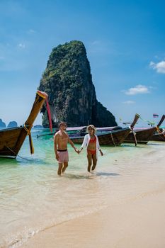couple mid age on tropical beach in Thailand, tourist walking on a white tropical beach, Railay beach with on the background lontail boat drop off tourist
