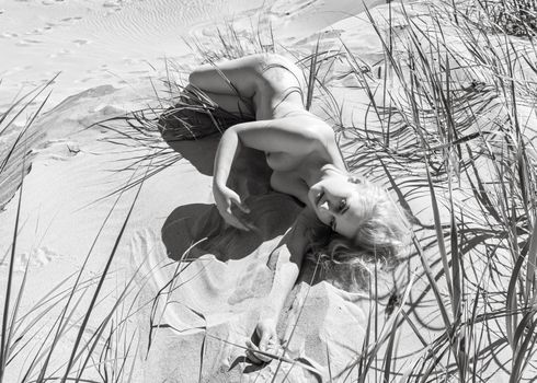 Lifestyle and beauty concept. Beautiful nude girl enjoying nature. Young naked blonde woman among the sand dunes on a sandy beach. Nude woman posing on sea beach.