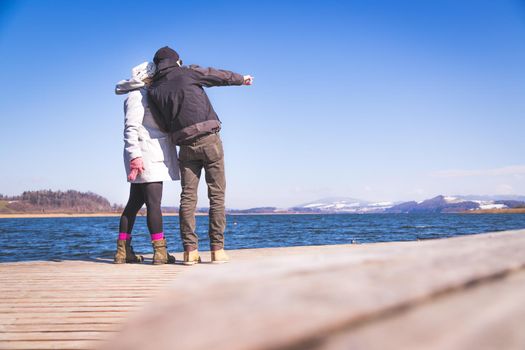 Happy young couple is standing on a footbridge and enjoying the view over the lake, winter time