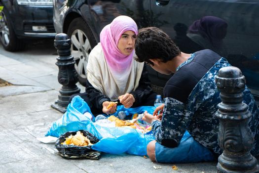 Poor muslim woman in hijab and man sit on sidewalk and eat leftovers