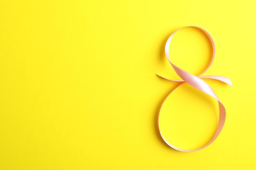 8 March, International Women's Day. Figure eight of pink ribbon on yellow background. Space for text