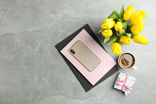 Beautiful tulips in vase and smartphone with accessories on gray background, top view
