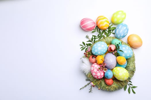 Flat lay composition with nest, Easter eggs, feathers and flowers on color background, space for text