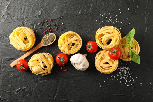 Flat lay composition with pasta, tomatoes, salt, garlic and spices on black background, space for text
