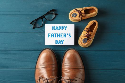 Brown leather shoes, children's shoes, inscription happy fathers day,  and glasses on wooden background, space for text and top view