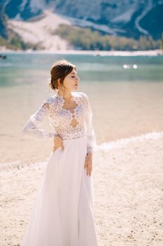 Beautiful bride in a white chiffon dress with sleeves and lace on the shore of Lake Lago di Braies in Italy. Destination wedding in Europe, on the popular Braies lake.