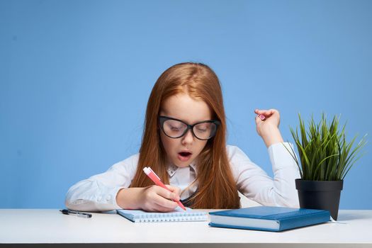 red-haired girl with glasses doing homework at the table school education. High quality photo