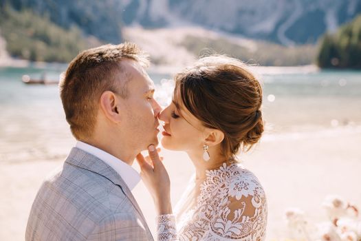 The newlyweds kiss on the spot for the ceremony, with an arch of autumn flower columns, against the backdrop of the Lago di Braies in Italy. Destination wedding in Europe, on Braies lake.