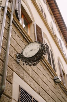 Vintage street clock on the wall of a building, with metal forged decoration.