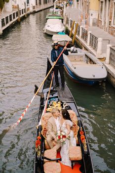 Venice, Italy - 04 october 2019: Italy wedding in Venice. A gondolier rolls a bride and groom in a classic wooden gondola along a narrow Venetian canal. Newlyweds are sitting in a boat