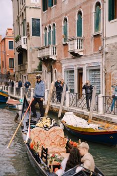 Venice, Italy - 04 october 2019: Italy wedding in Venice. A gondolier rolls a bride and groom in a classic wooden gondola along a narrow Venetian canal. Newlyweds are sitting in a boat and kissing.