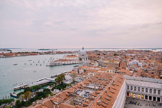 Aerial view from huge cathedral bell tower St Mark's Campanile on Santa Maria - Della - Salute - Church in the name of St. Mary the Savior, sunset sky and orange roof tiles. Venice, Italy